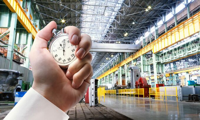 Hintergrund Fertigungshalle in einem Industriebetrieb, Vordergrund: Hand mit einer Stoppuhr